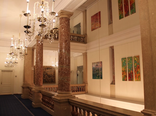 Un vestíbulo imponente con columnas de mármol, una araña y obras de arte en las paredes.
