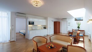 A modern living room with a sofa, chairs, a wooden coffee table with fruit, and a kitchen in the background.