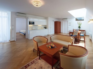 Una sala de estar moderna con un sofá, sillas, una mesa de centro de madera con fruta y una cocina al fondo.