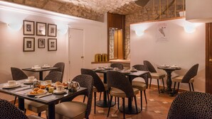 A dining area with tables and chairs, a stone ceiling, and framed pictures on the wall. - Crystal Hôtel (Paris)