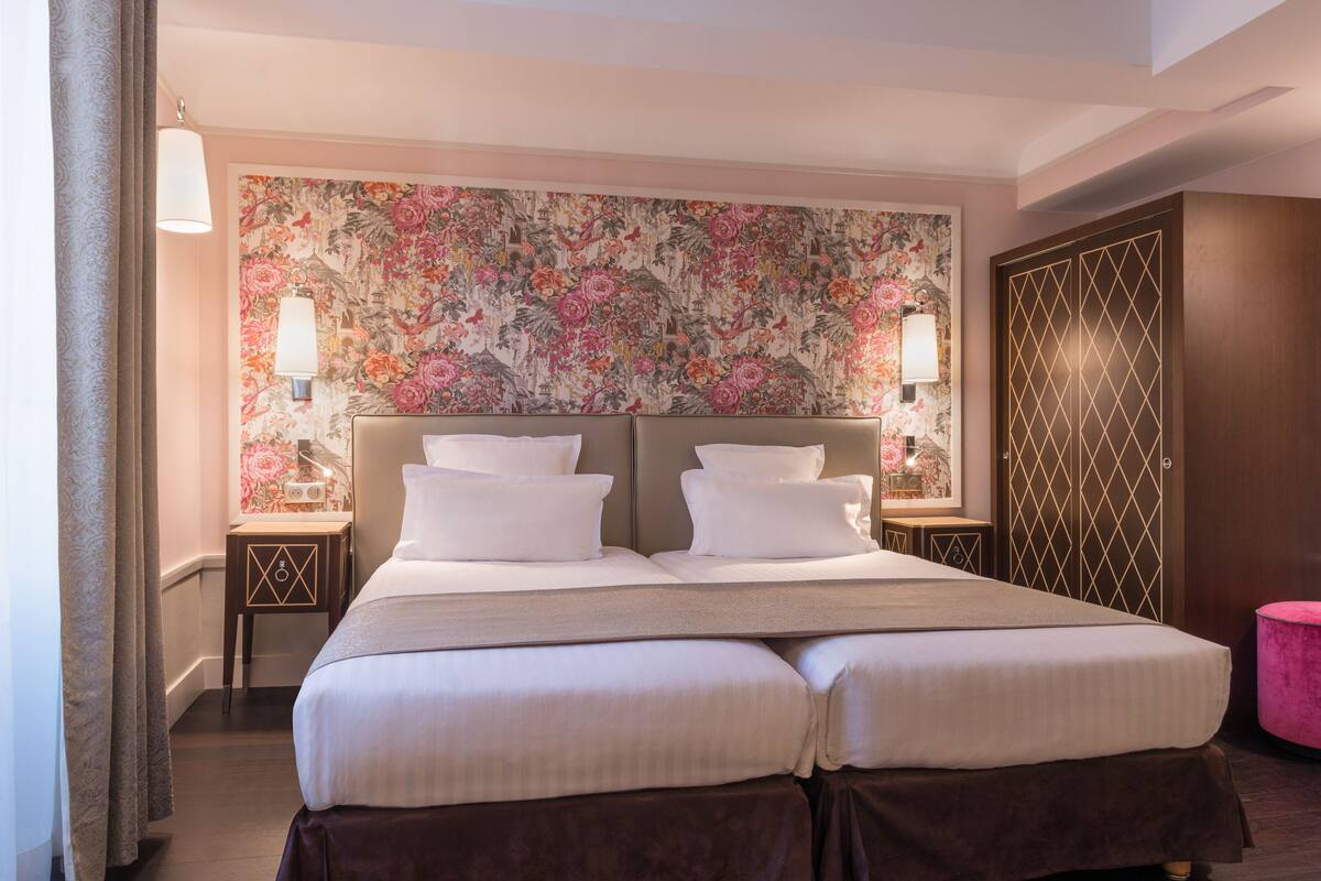 A double bed with a floral headboard, two bedside lamps, and a wooden wardrobe.