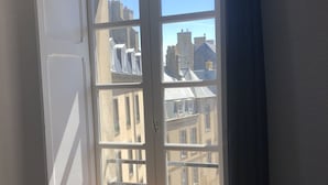 A room with a large window overlooking a cityscape, featuring a view of buildings and a clock tower. - Hôtel Elizabeth (Saint-Malo)