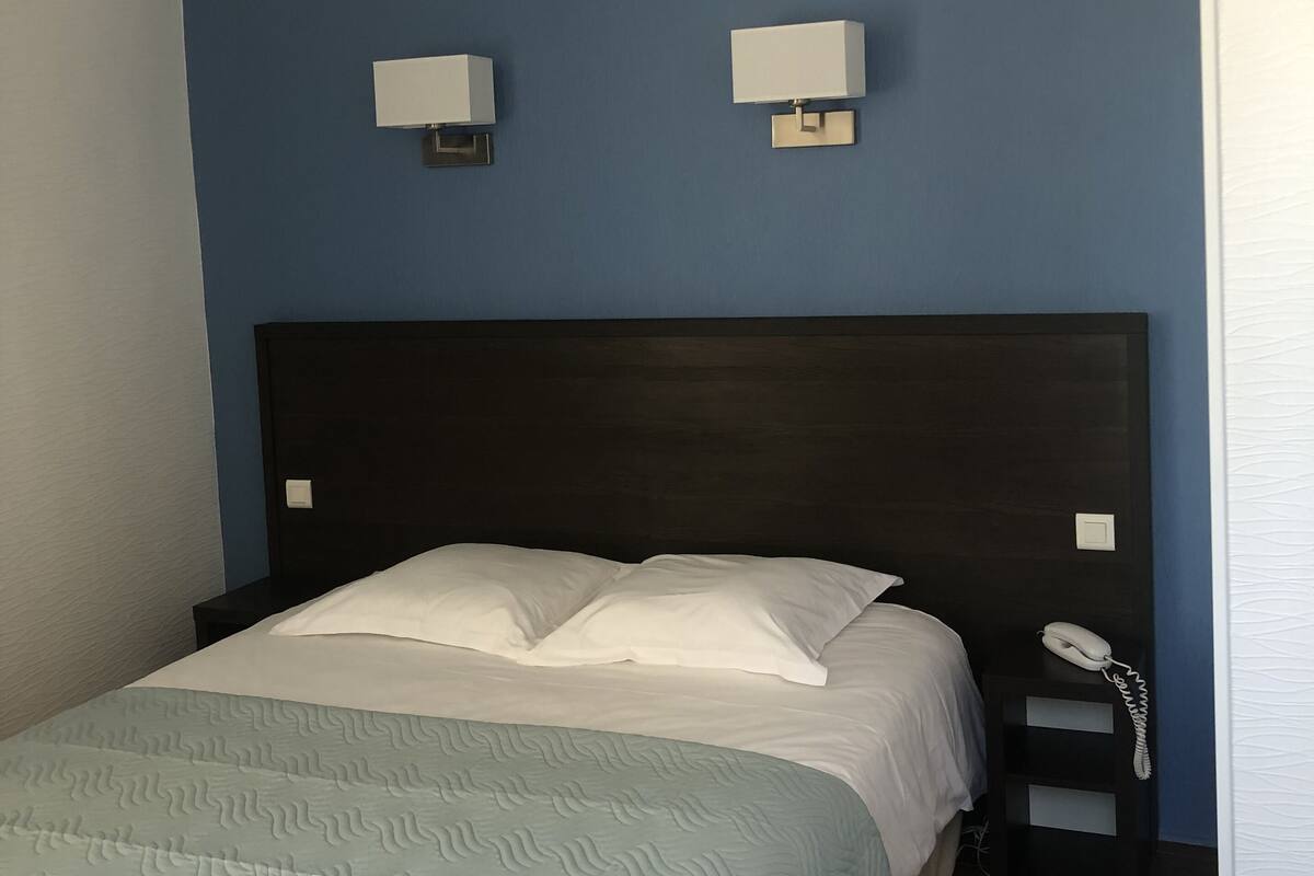 A hotel room with a bed, two wall-mounted lights, a bedside telephone, and a nightstand.
