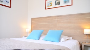 A neatly made bed with white linens and two blue pillows, a wooden headboard, and bedside lamps. - Hôtel Elizabeth (Saint-Malo)