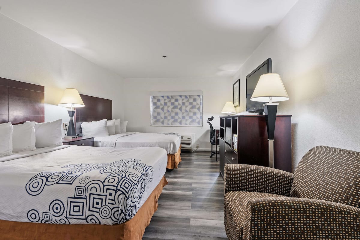 Habitación de hotel con dos camas, un sofá, un televisor y un papel tapiz estampado.