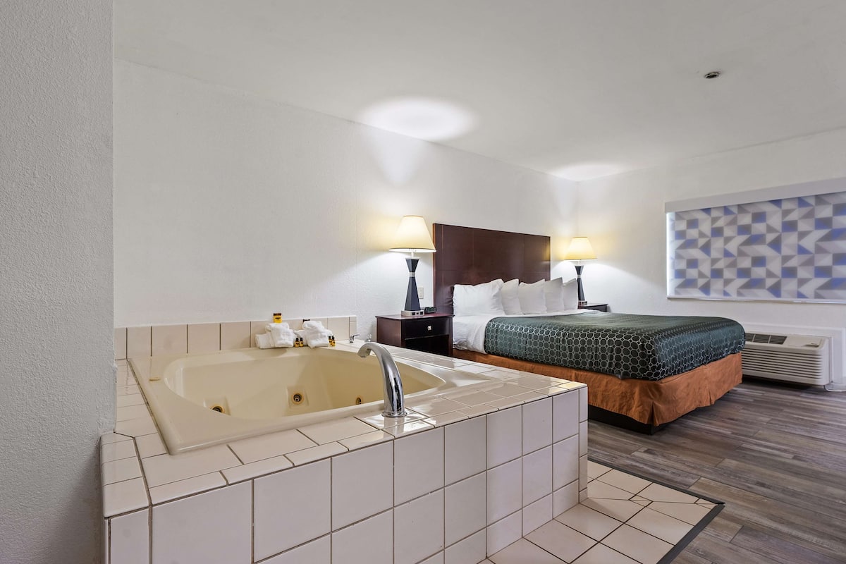 Habitación de hotel con una bañera grande, una cama con cubrecama verde y naranja, dos lámparas de noche y un aire acondicionado de pared.