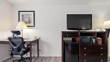 Une chambre d’hôtel équipée d’un bureau, d’un fauteuil de bureau noir, d’un téléviseur posé sur un meuble en bois, d’un four à micro-ondes et d’une lampe.
