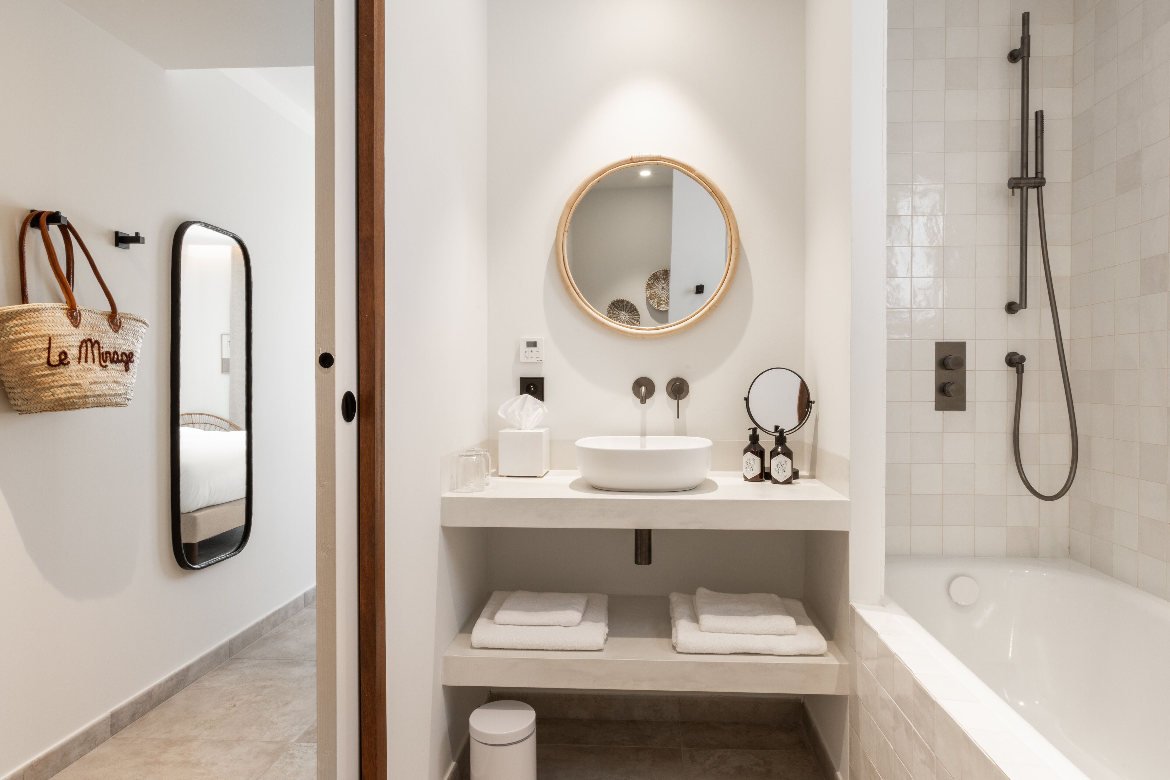 A modern bathroom with a round mirror, a white sink, and a bathtub. There are towels and toiletries on the counter.