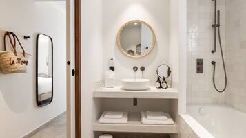 A modern bathroom with a round mirror, a white sink, and a bathtub. There are towels and toiletries on the counter.