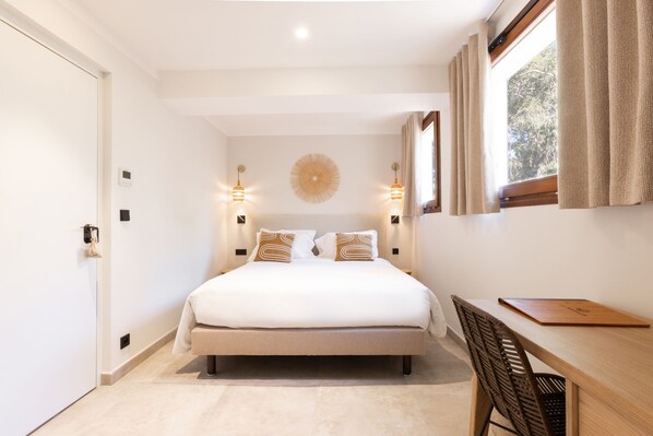A bedroom with a bed, bedside lamps, a desk, and a window with curtains. - Le Mirage (Bormes-Les-Mimosas)