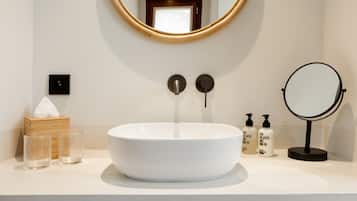 Une salle de bain avec un miroir rond, un lavabo blanc et deux serviettes rangées sous le lavabo.