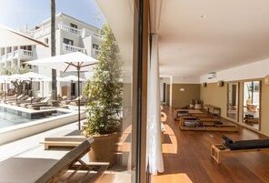Una habitación de hotel moderna con piscina, tumbonas, estudio de Pilates y un amplio ventanal con vistas a la zona de la piscina.