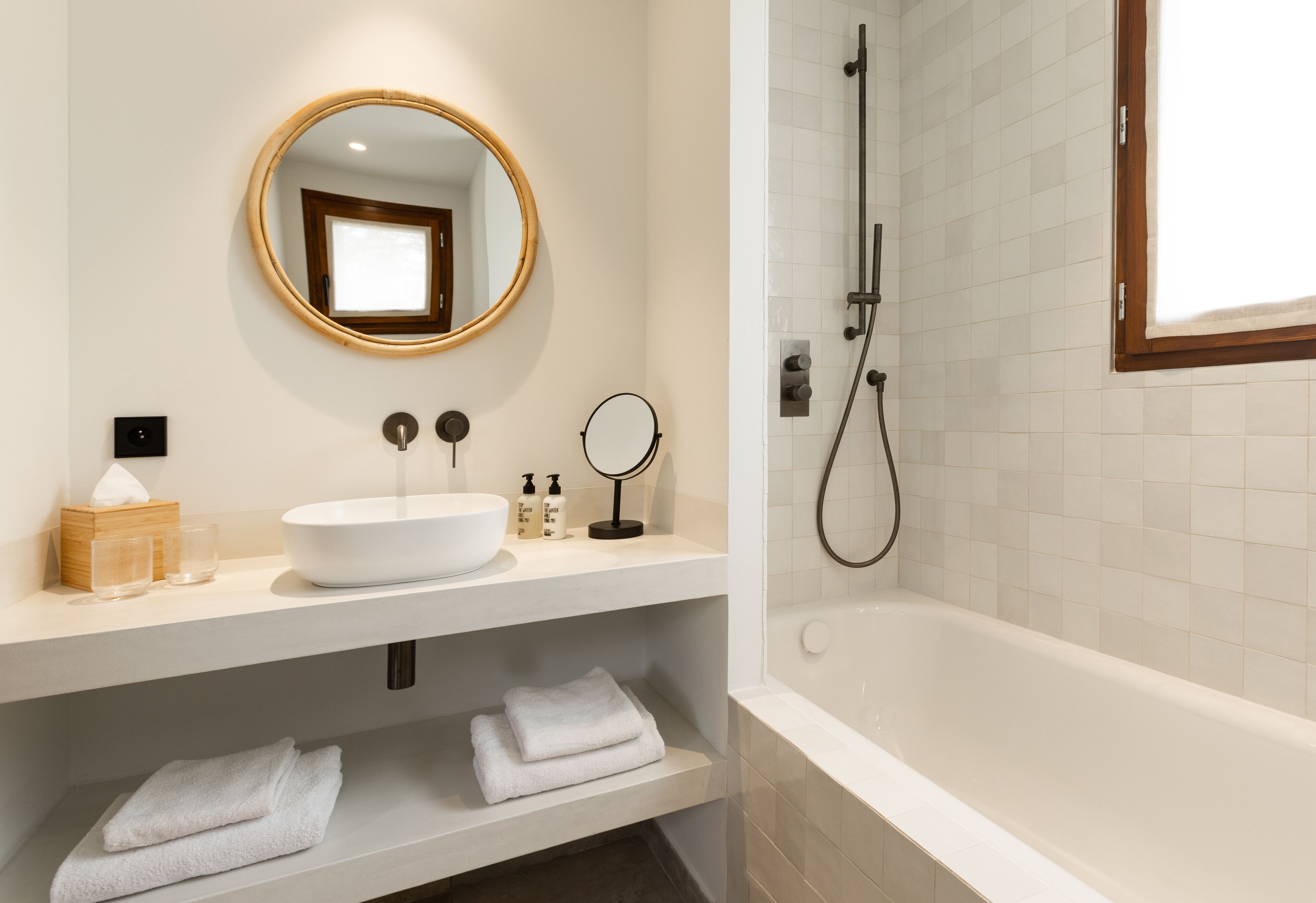 Een moderne badkamer met een witte wastafel, ronde spiegel en een bad.