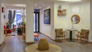 Un salon moderne avec un pouf rond en cuir, deux fauteuils en bois, une petite table et un tableau encadré accroché au mur.