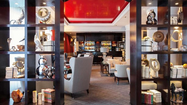Un vestíbulo de hotel con zona de bar, estanterías decoradas con objetos y una pared de acento roja.