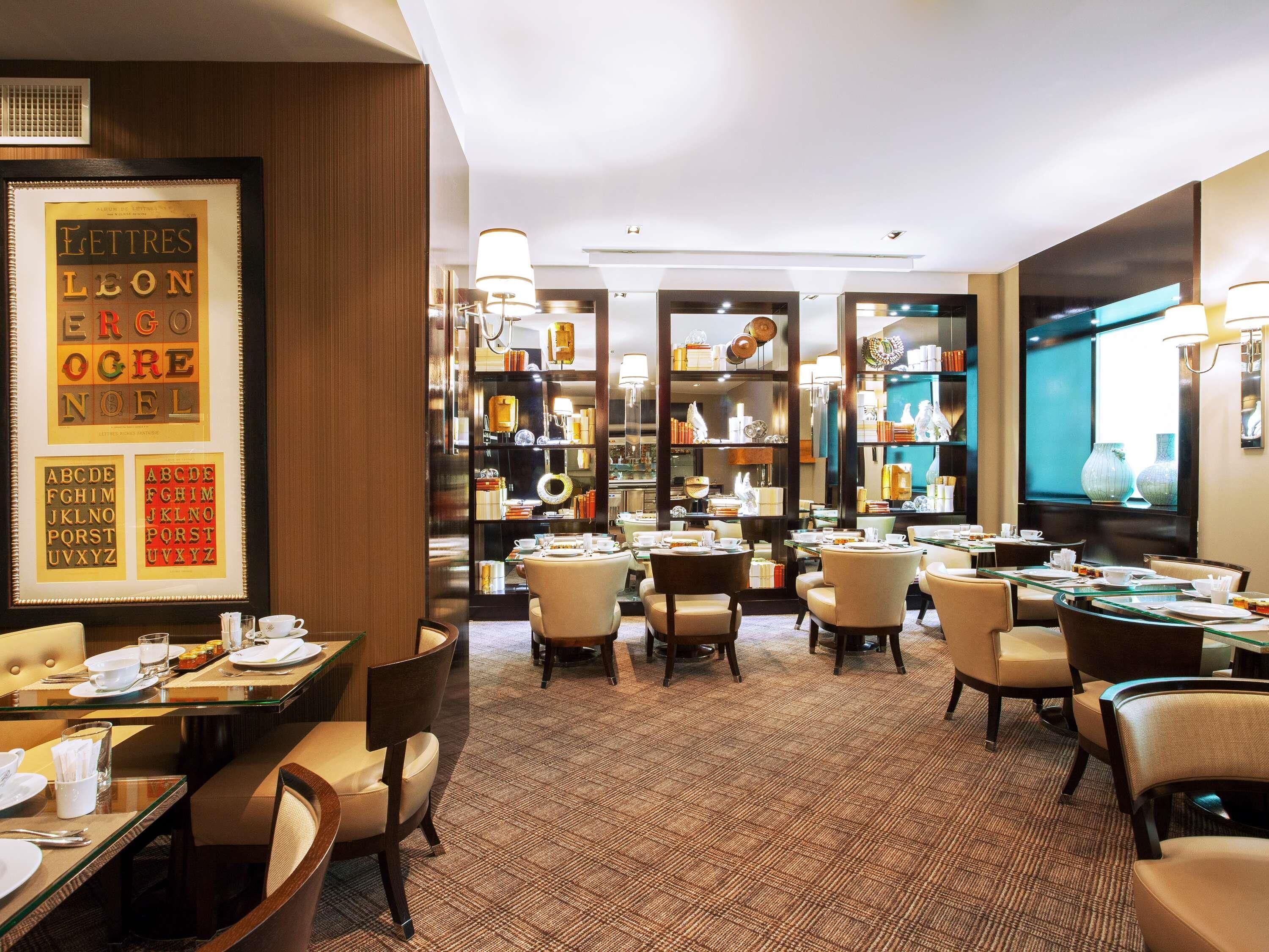 A hotel dining area with tables set for service, framed alphabet art on the wall, and a patterned carpet.