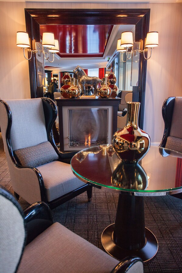 A hotel room with a glass-top table, two armchairs, a fireplace, and wall-mounted lamps. - Park Hotel Grenoble - Handwritten Collection (Grenoble)