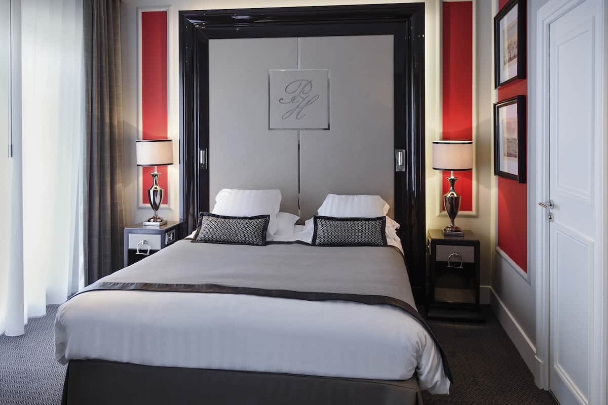 Una habitación de hotel con una cama grande, dos mesitas de noche, una pared de acento roja y una obra enmarcada sobre la cama.