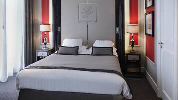 Una habitación de hotel con una cama grande, dos mesitas de noche, una pared de acento roja y una obra enmarcada sobre la cama.