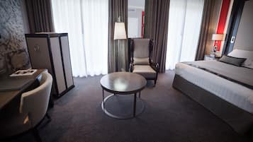 A hotel room with a bed, a desk, a chair, a round table, and a lamp.