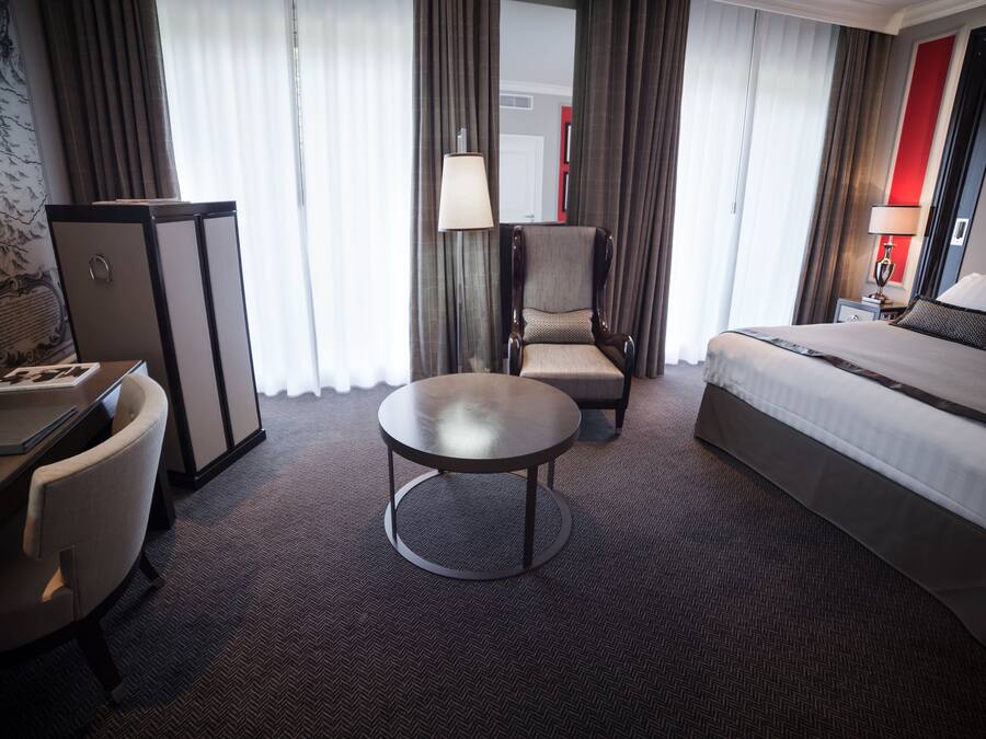 A hotel room with a bed, a desk, a chair, a round table, and a lamp.