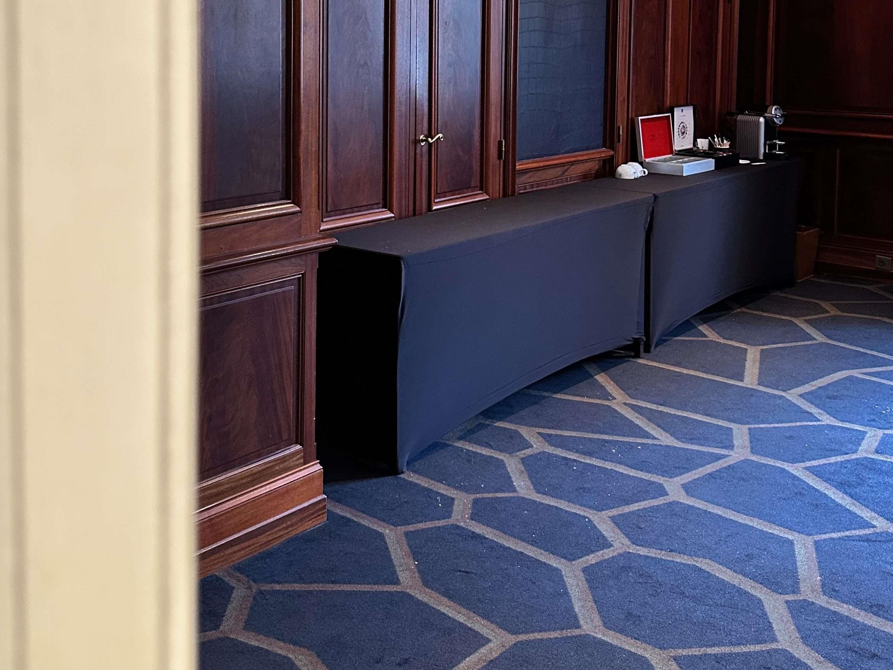 Una habitación de hotel con alfombra azul oscuro, armarios de madera y una mesa cubierta con mantel negro.