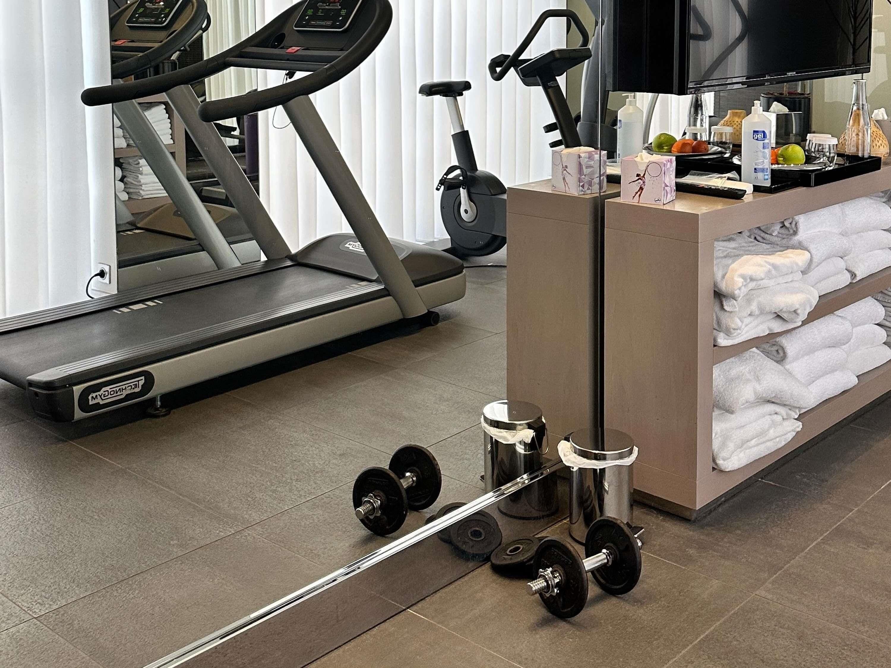 Un espacio de gimnasio con una cinta de correr, una bicicleta estática, un banco de pesas y un perchero para toallas.