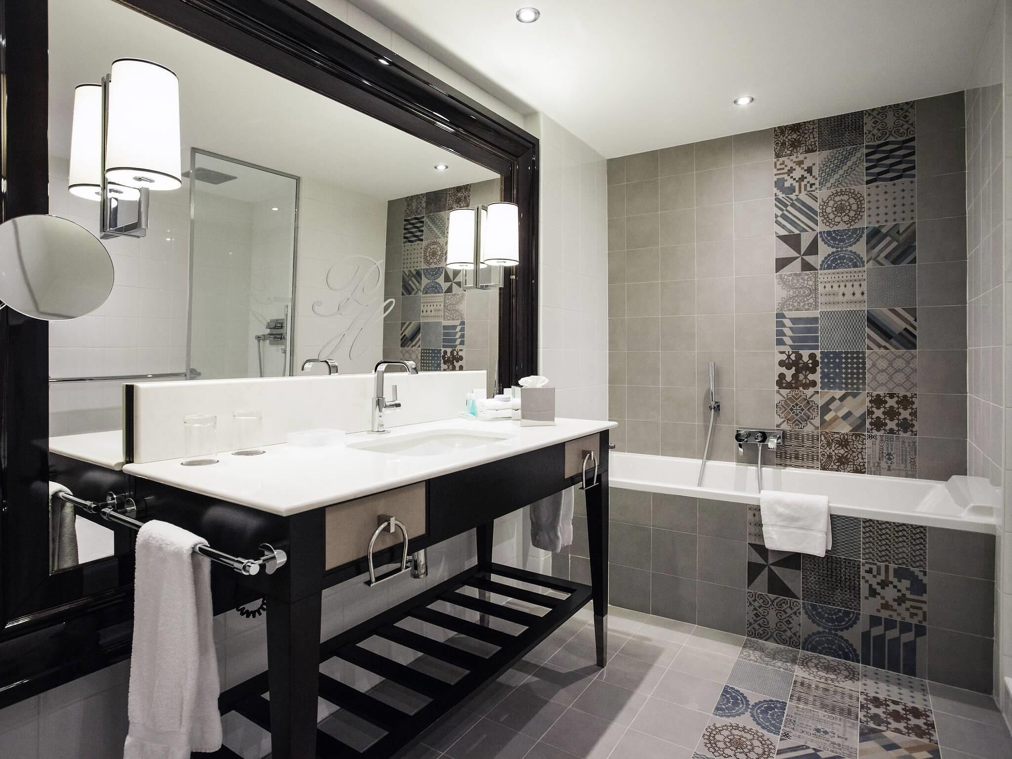 A modern bathroom with a large mirror, a sink, a bathtub, and patterned tiles.
