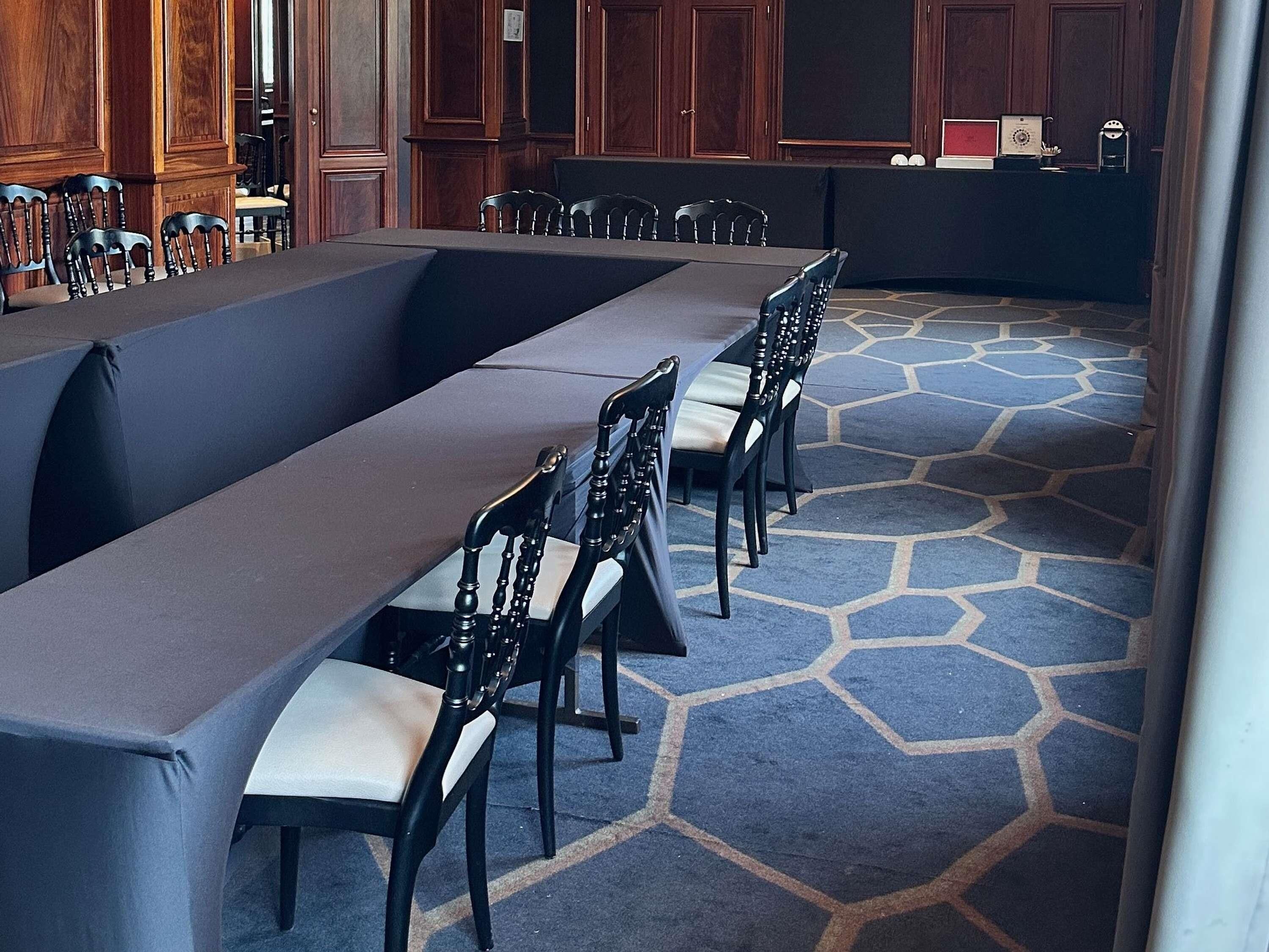 A conference room with a long table and chairs, wooden paneling, and a patterned carpet.