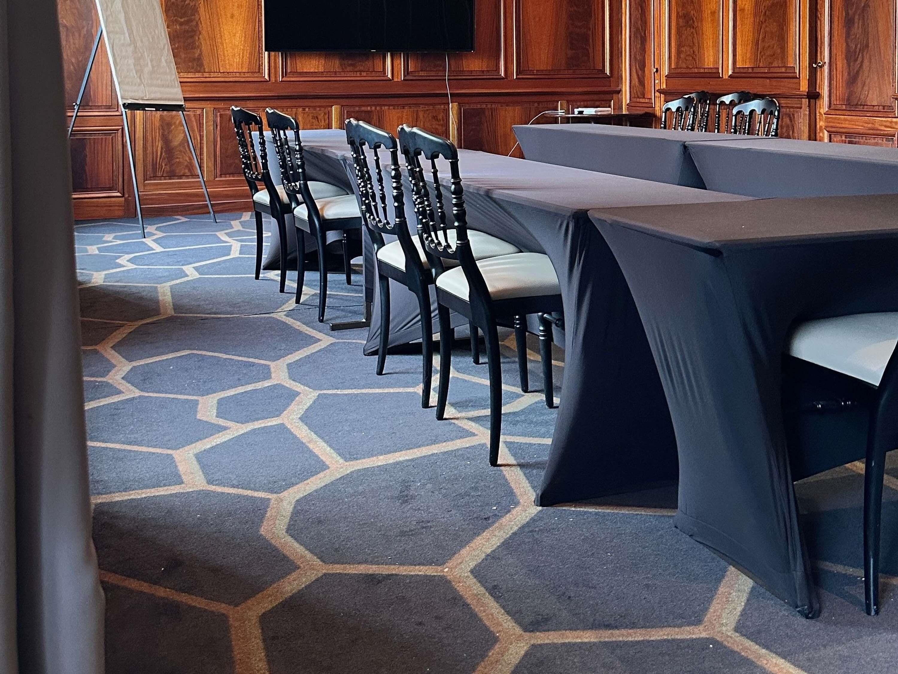 A conference room with a long table, chairs, a projector screen, and a carpet with a geometric pattern.