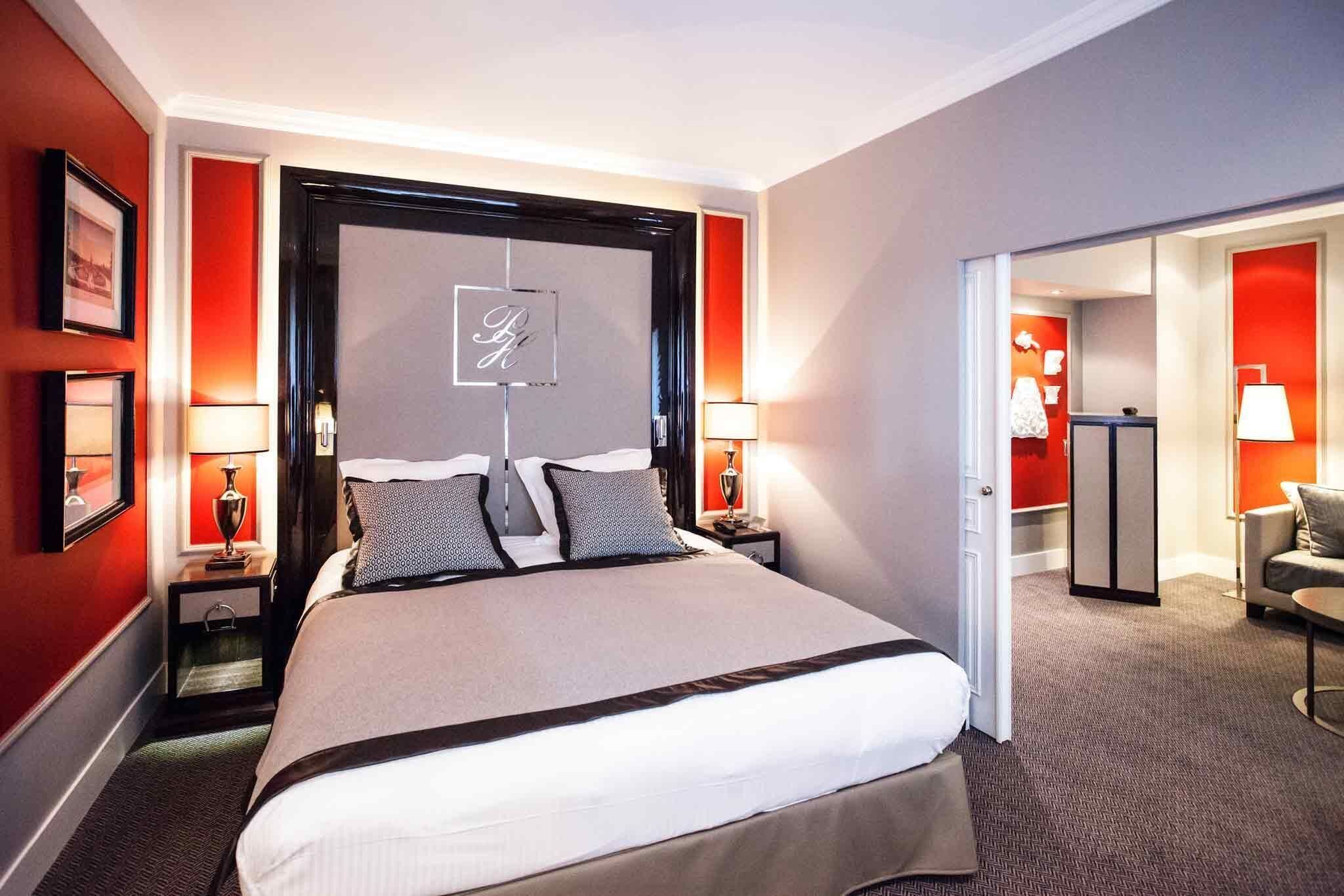 A hotel room with a large bed, bedside tables with lamps, a framed picture, and a door leading to another room.