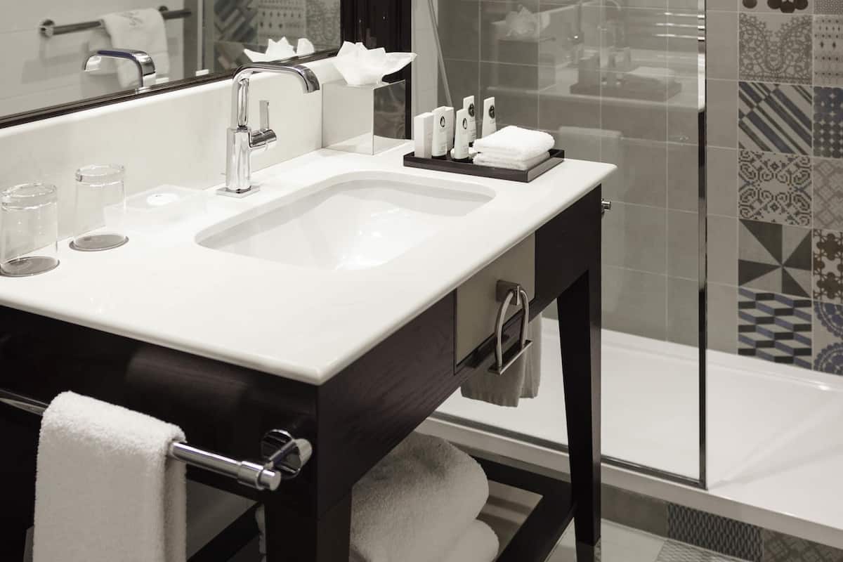 Un baño moderno con un lavabo blanco, un espejo, un perchero para toallas y una cabina de ducha de cristal.