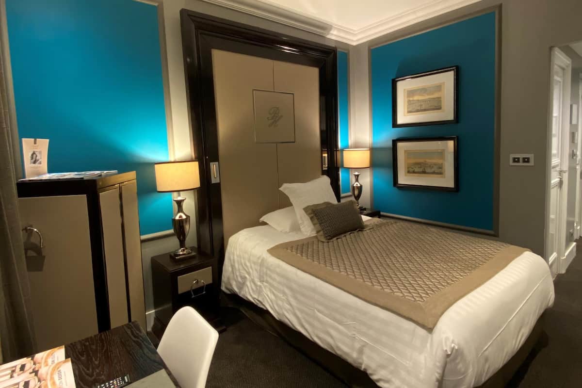 Habitación de hotel con cama, lámparas de noche, escritorio y armario.