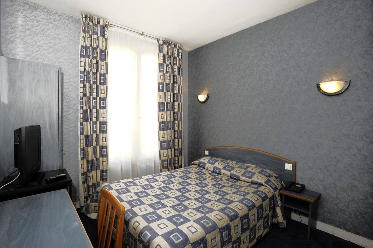 Een hotelkamer met een bed, een bureau met televisie, een stoel, een nachtkastje en een raam met gordijnen.