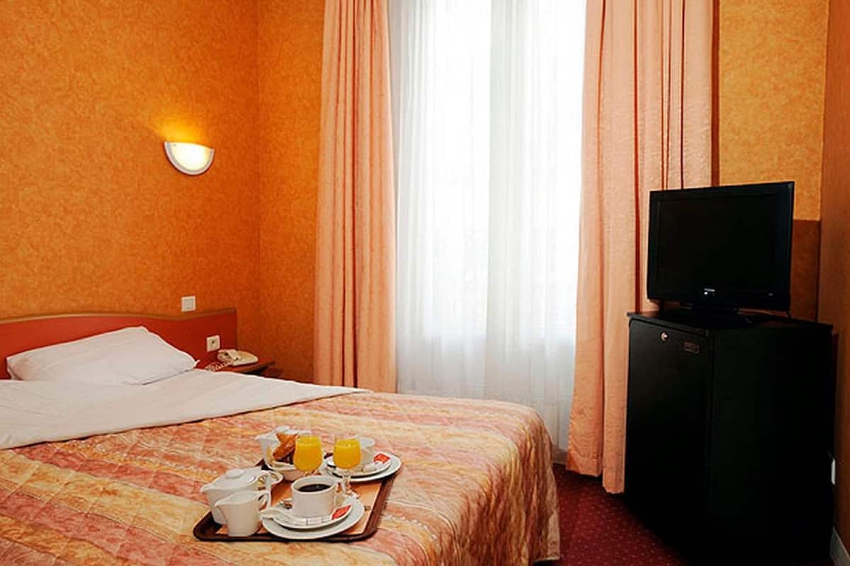 Een hotelkamer met een bed, een televisie, een klein kastje en een ontbijttray met sinaasappelsap en koffie.