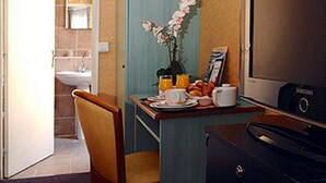 Une chambre d’hôtel de taille réduite comprenant un petit coin repas, une chaise, une table avec des articles pour le petit-déjeuner, un téléviseur et un meuble de rangement.