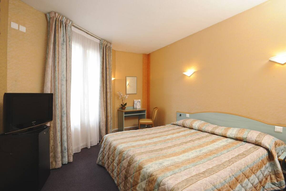Een hotelkamer met een bed, een bureau, een stoel, een televisie en een raam met gordijnen.