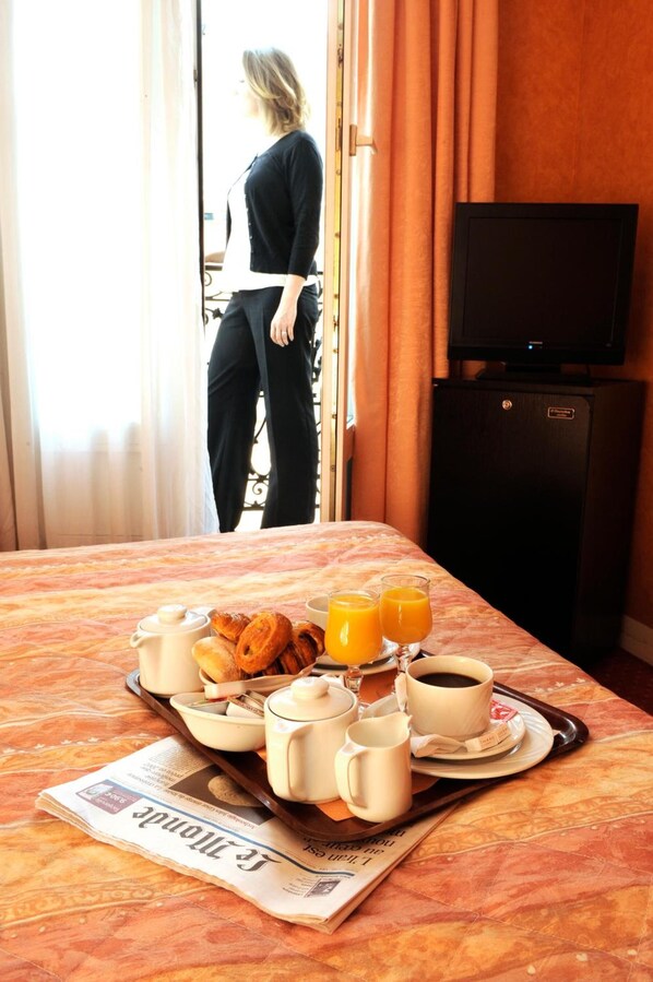 Une chambre d’hôtel avec un plateau de petit-déjeuner sur le lit, comprenant des croissants, du café et du jus d’orange.
