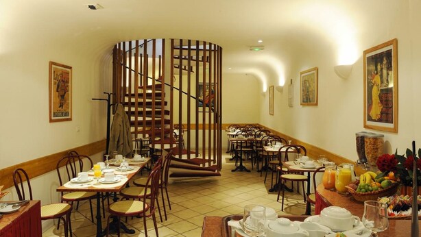 Un espace repas avec plusieurs tables préparées pour le petit-déjeuner, un escalier central en colimaçon et diverses œuvres d’art accrochées aux murs.