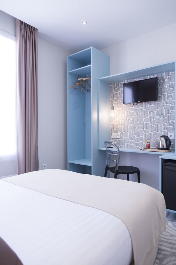 A hotel room with a bed, a desk with a chair, a TV, and a wardrobe.