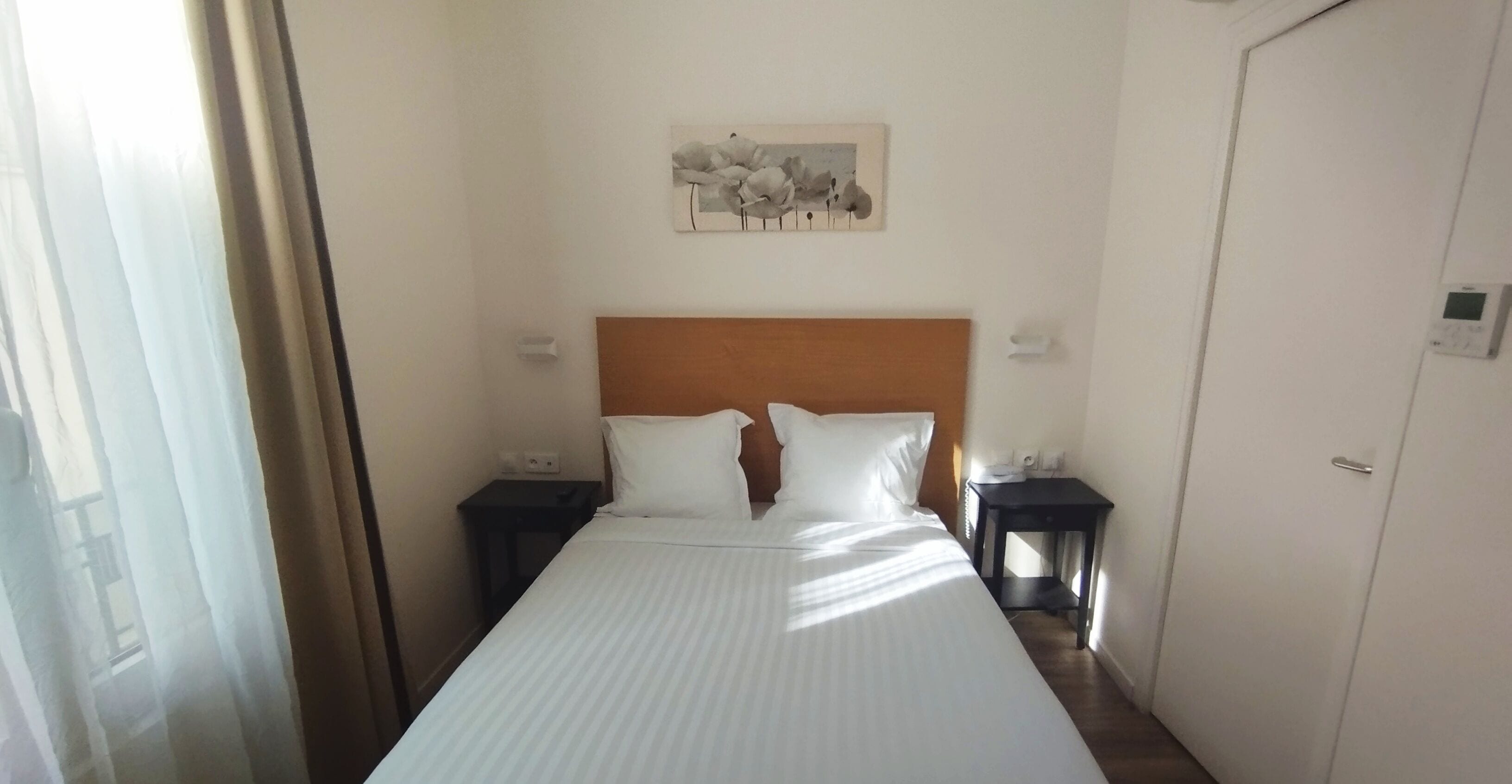 A hotel room with a large bed, two bedside tables, a wooden headboard, and a wall-mounted artwork.
