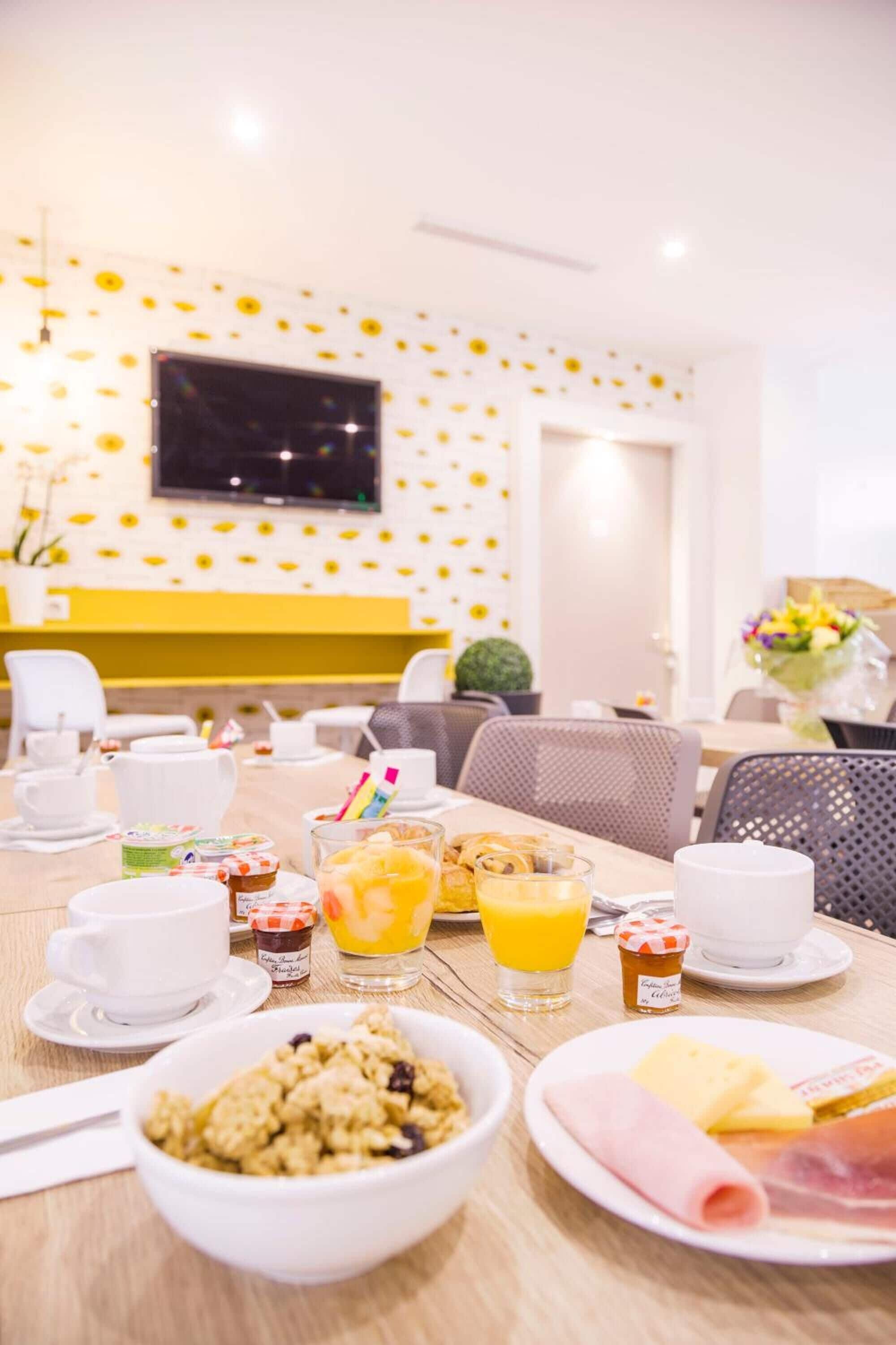 A breakfast setting with a table set for two, including plates of food, cups, and a glass of orange juice.