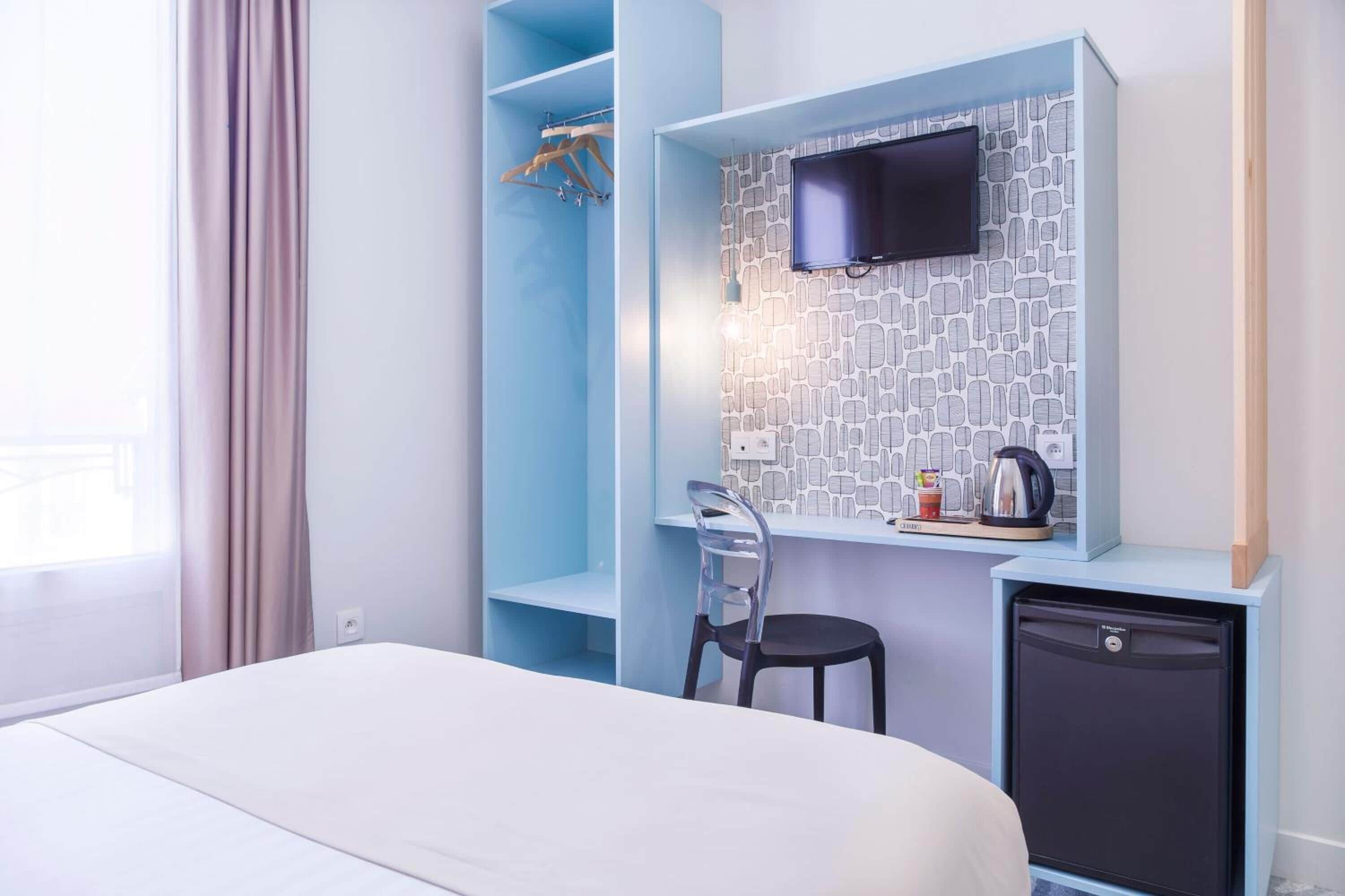Una habitación de hotel con cama, escritorio, silla, televisor y refrigerador pequeño.