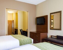 Quarto de hotel com duas camas, uma escrivaninha, uma cadeira, uma televisão, um armário e um espelho.