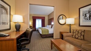 A hotel room with a desk, two chairs, a bed, a sofa, and a mirror. - Russell Inn & Suites (Starkville)