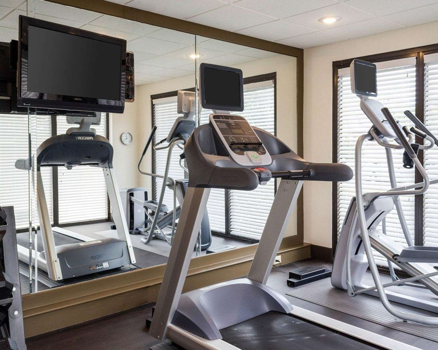 A fitness center with treadmills, a mirrored wall, and a television mounted on the wall.