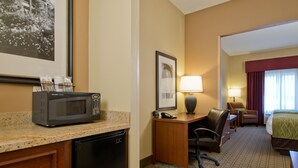 A hotel room with a microwave on the counter, a desk with a lamp, a chair, and a bed. - Russell Inn & Suites (Starkville)