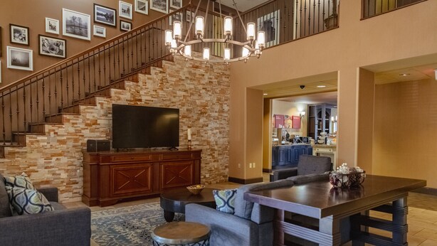 A spacious living area with a staircase, a flat-screen TV, a dining table, and a kitchen in the background. - Russell Inn & Suites (Starkville)