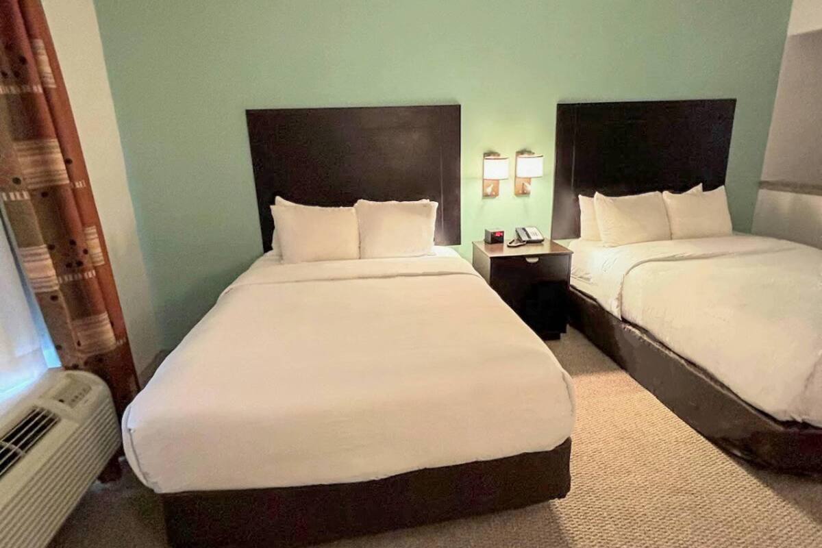 A hotel room with two beds, a nightstand with a phone, and a wall-mounted lamp.