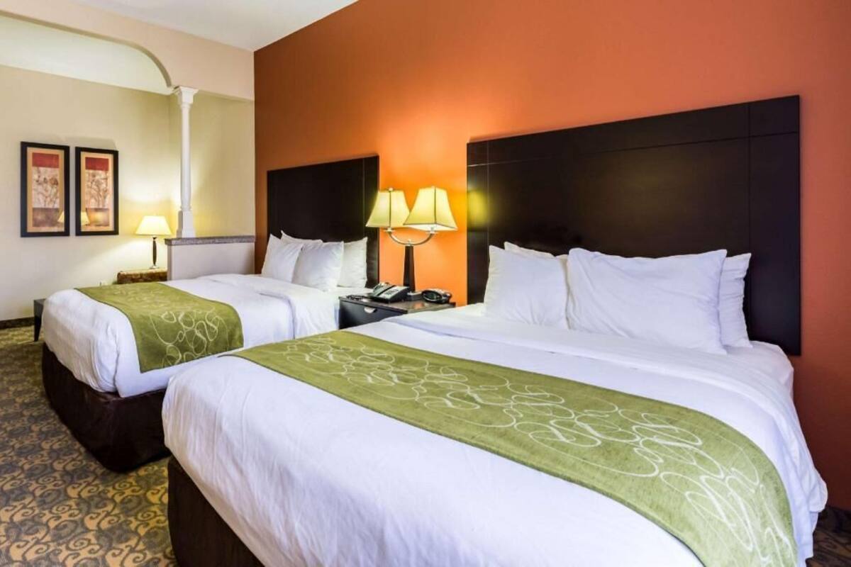 A hotel room with two beds, a nightstand with a lamp, and a wall-mounted telephone.